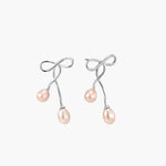 Rhodium-plated silver earrings with organic vine curves and two peachy freshwater pearls on cream background
