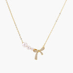 Delicate gold necklace with three white pearls and crystal-embellished bow pendant on cream background