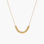 Delicate gold-plated necklace with graduated spherical beads forming gentle smile curve on beige background