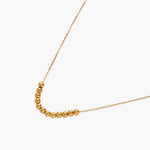 Delicate gold-plated necklace with graduated spherical beads forming gentle smile curve on beige background
