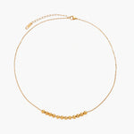Delicate gold-plated necklace with graduated spherical beads forming gentle smile curve on beige background