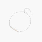 Delicate rhodium-plated silver chain bracelet with row of small baroque pearls centered on white background.