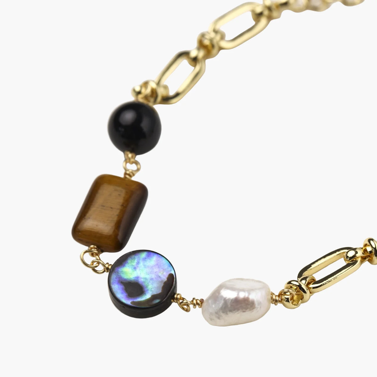 Gold chain bracelet with tiger's eye, obsidian, pearl, and iridescent abalone stones on cream background.