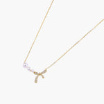 Delicate gold necklace with three white pearls and crystal-embellished bow pendant on cream background