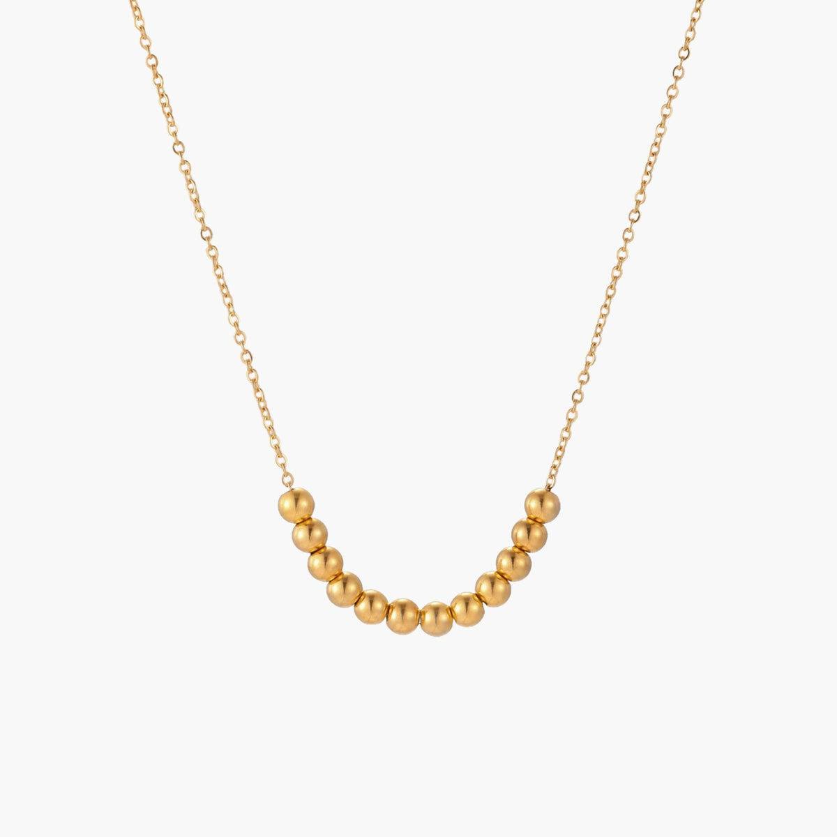 Delicate gold-plated necklace with graduated spherical beads forming gentle smile curve on beige background